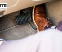 A mechanic sitting in the back seat of a car wearing brown shoes.