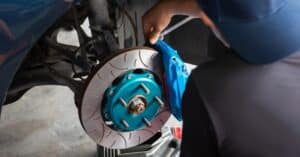 A mechanic in West Jordan, Utah, is meticulously inspecting a vehicle's disc brake system for brake repair, focusing on the rotor and caliper, in a bustling garage setting.