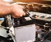 Mechanic testing a car battery with diagnostic tools in a repair shop.