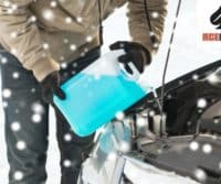 A mechanic is pouring water into a car in the snow for auto repair.