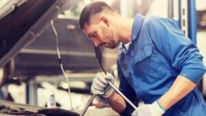 A mechanic in a blue jumpsuit and gloves works under the hood of a car, handling driveline repair in an auto repair shop in South Salt Lake, UT.