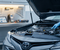 A person wearing gloves inspects the engine of a Toyota car in an auto repair shop, where tools and diagnostic equipment reflect a transparent approach to servicing often valued by family car owners.